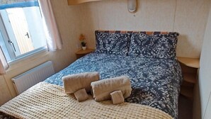 A bedroom with a bed, a window, a radiator, and a nightstand with a lamp. - Comfortable Mobile Home in the Countryside (Birra)