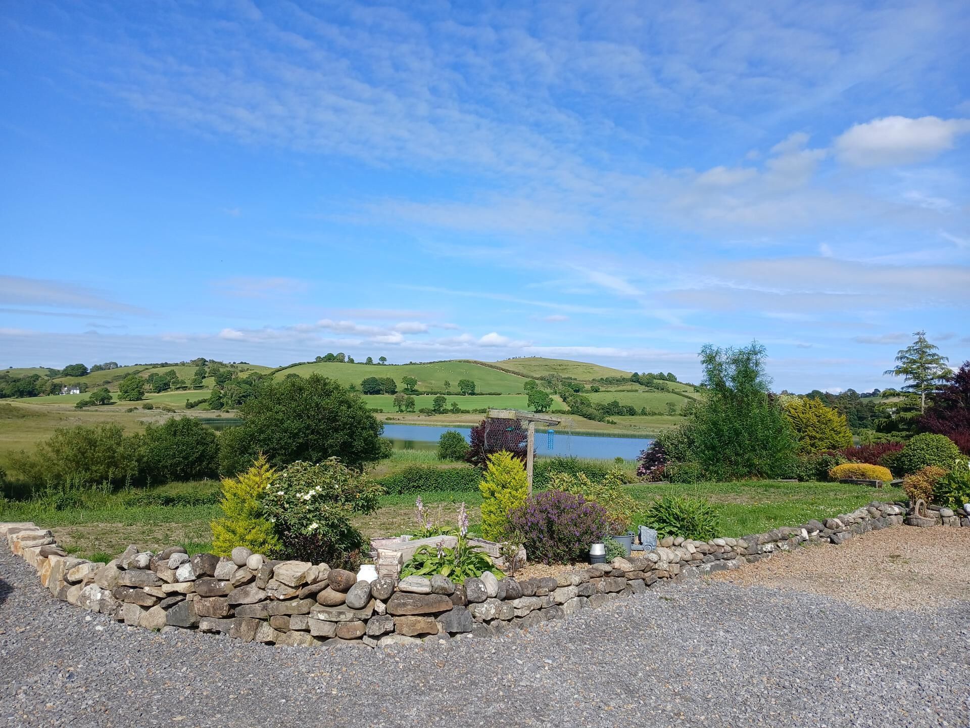 A rural landscape with a stone wall, a pond, and rolling hills in the background.