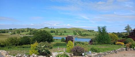 A rural landscape with a stone wall, a pond, and rolling hills in the background.