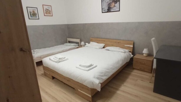 A room with two single beds, a wooden headboard, a nightstand with a lamp, and a small black cabinet. - Aria di Sale Hostel (Trieste)