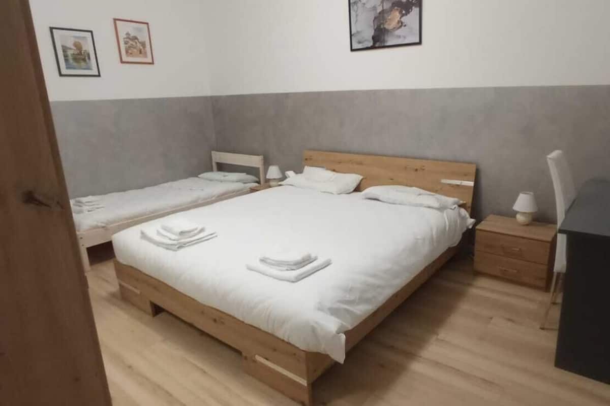 Une chambre avec deux lits simples, une tête de lit en bois, une table de chevet avec une lampe et une petite armoire noire.