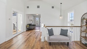 Ein geräumiger Wohnbereich mit Holzboden, grauem Sofa mit Kissen, weißer Geländer und einer Pendelleuchte.