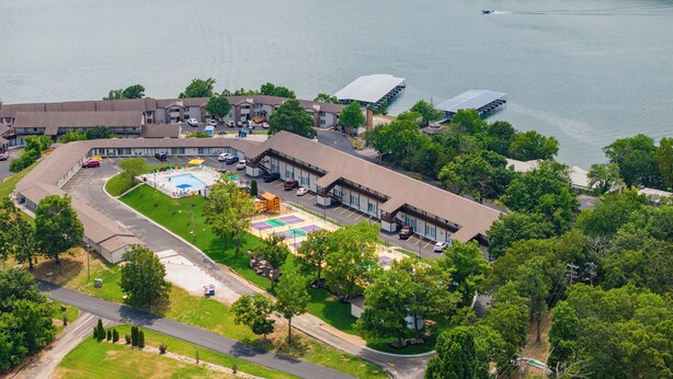 An aerial view of a hotel with a large swimming pool, tennis courts, and a boat dock.