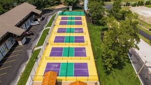 An aerial view of a sports facility with multiple tennis courts, a parking area, and a small wooden structure.