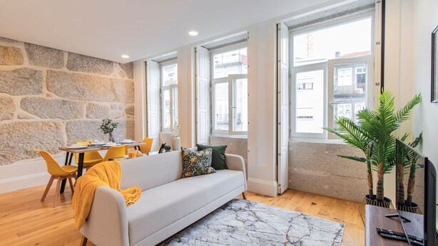 A modern living room with a stone wall, a sofa, a dining table, and a large window.
