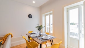 A dining area with a wooden table, yellow chairs, a clock on the wall, and a window with a view. - Rodrigues de Freitas 391 2J by LovelyStay (Porto)