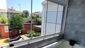 A modern bathroom with a large bathtub, a window with blinds, and a view of the outside. - Artof  Alaçatı (Çesme)