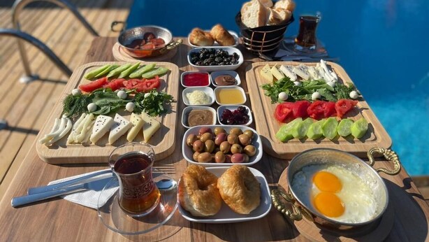 A table with various food items and a glass of tea, set outdoors by a pool. - Artof  Alaçatı (Çesme)