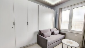 A modern room with a grey sofa, a small round table, and a large wardrobe. - Pretty Petitie Fully Equipped City Center Studio (Thessaloniki)