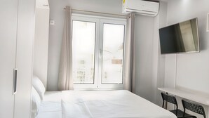 A hotel room with a bed, a TV mounted on the wall, and a window with curtains. - Pretty Petitie Fully Equipped City Center Studio (Thessaloniki)