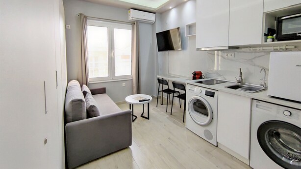 A compact kitchen with a washing machine, a microwave, and a small dining area with two chairs. - Pretty Petitie Fully Equipped City Center Studio (Thessaloniki)