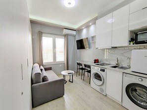 A compact kitchen with a washing machine, a microwave, and a small dining area with two chairs.
