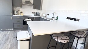 Une cuisine moderne avec des meubles gris, un plan de travail blanc et un îlot central intégré, agrémenté de tabourets de bar.
