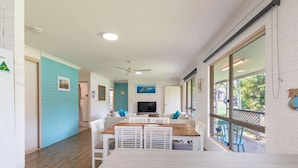 A modern kitchen with white cabinetry, a dining area with a wooden table and white chairs, and a large window with a view of the outdoors.