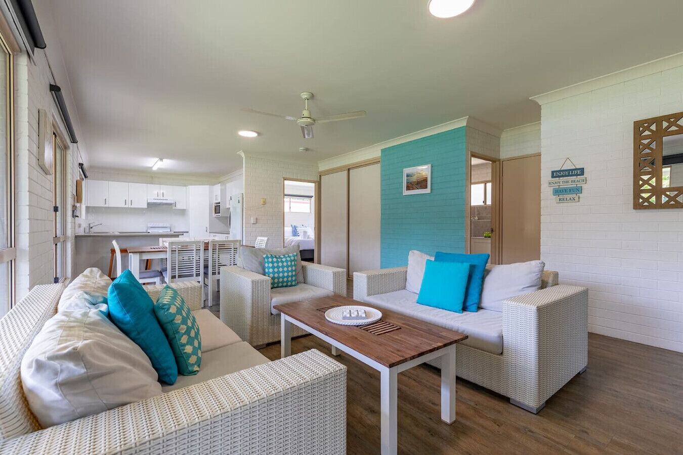 A modern, well-lit living area with wicker furniture, a wooden coffee table, and a kitchen in the background.