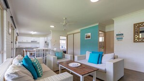 A modern, well-lit living area with wicker furniture, a wooden coffee table, and a kitchen in the background.