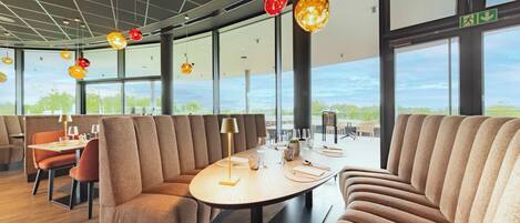 Un restaurant moderne avec de hauts plafonds, de grandes fenêtres et une table à manger centrale entourée de banquettes confortables.