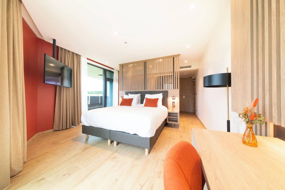 A modern hotel room with a large bed, a desk, and a flat-screen TV mounted on the wall.