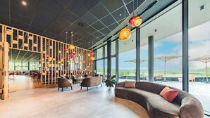 A modern interior with a curved sofa, seating area, and large windows offering a view. - Hotel du Bois d'Arlon (Arlon)