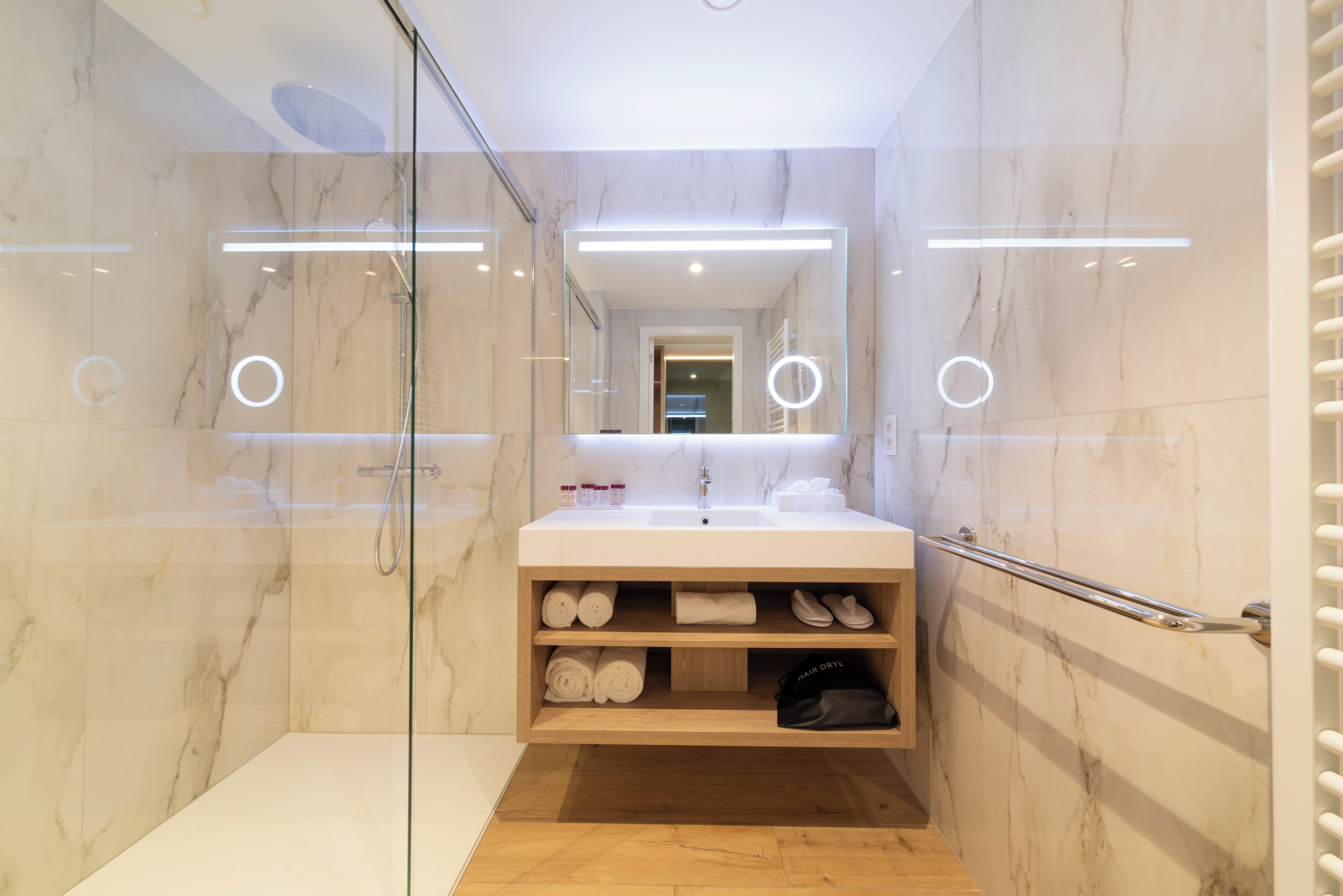 Un baño moderno con cabina de ducha de vidrio, tocador con espejo y estantes empotrados para toallas y artículos de aseo.