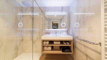 Un baño moderno con cabina de ducha de vidrio, tocador con espejo y estantes empotrados para toallas y artículos de aseo.