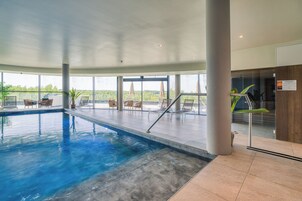 Una piscina interior con vistas despejadas al exterior, rodeada de sillones de descanso y una barandilla de cristal.