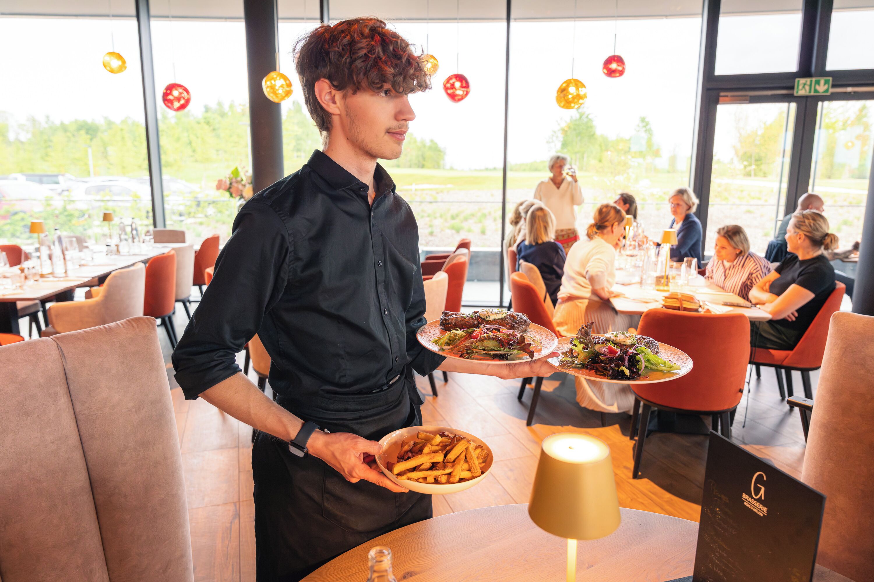 Een restaurantinterieur met tafels, stoelen en een ober die gerechten serveert.