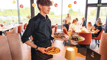 Een restaurantinterieur met tafels, stoelen en een ober die gerechten serveert.