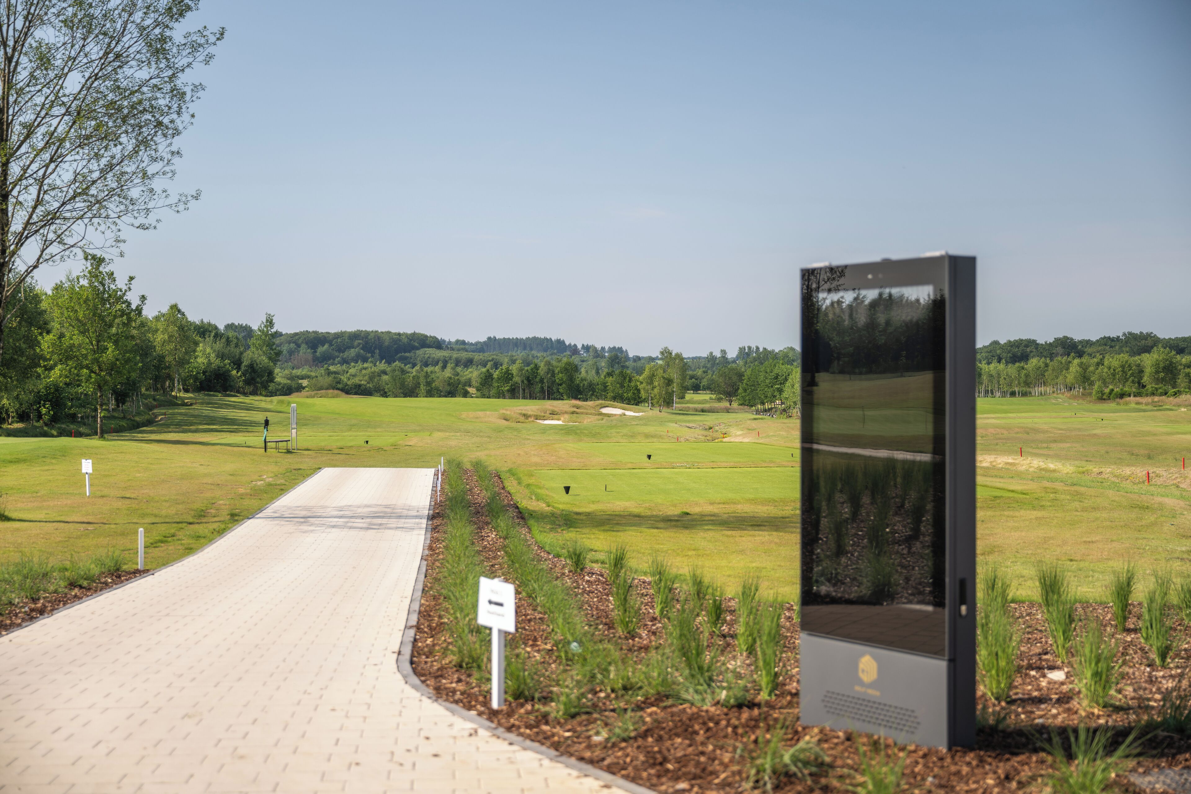 Un sendero pavimentado que conduce a un campo de golf con un panel de exhibición digital.