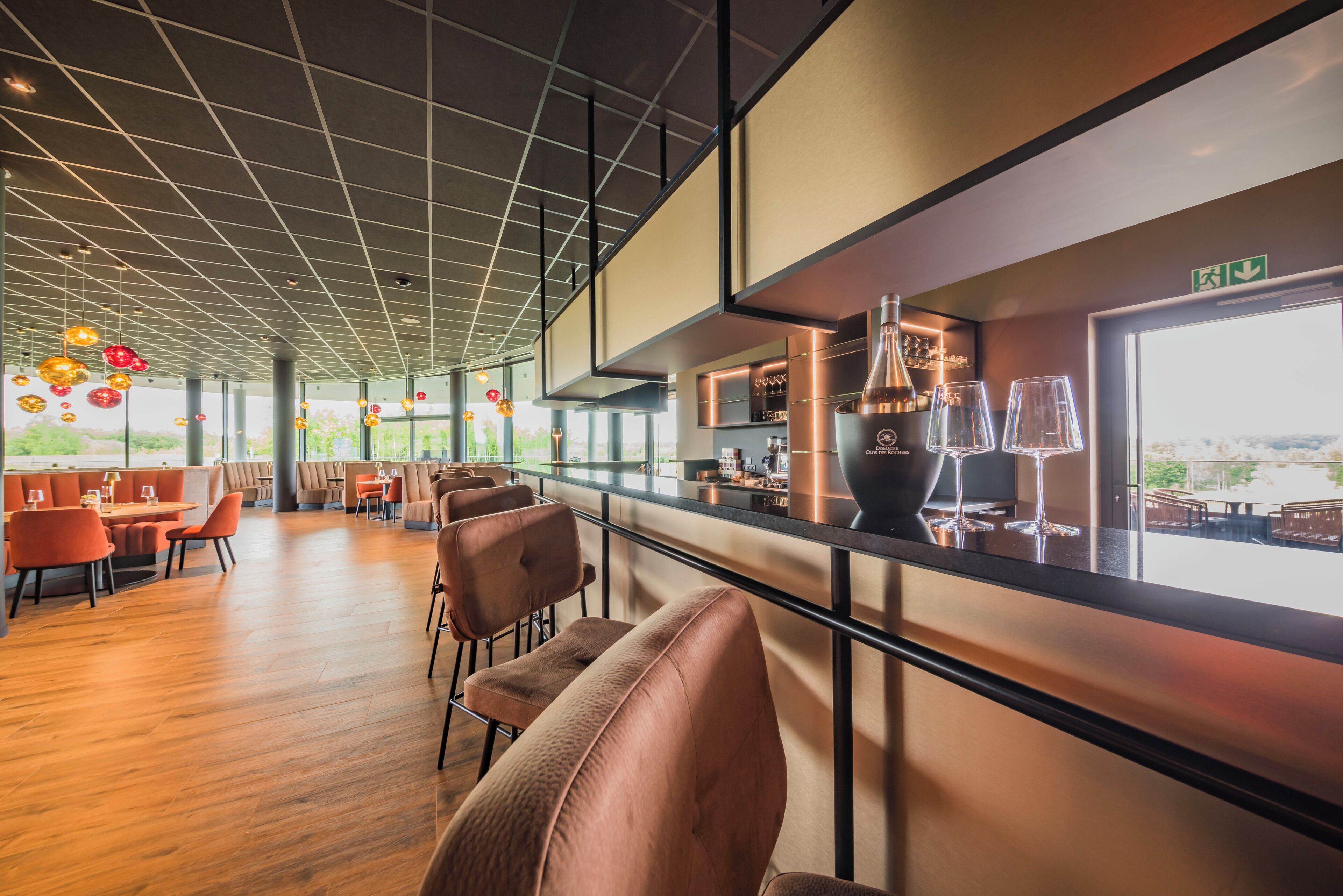 A modern restaurant with a bar area, wooden flooring, and a view of the outdoors.