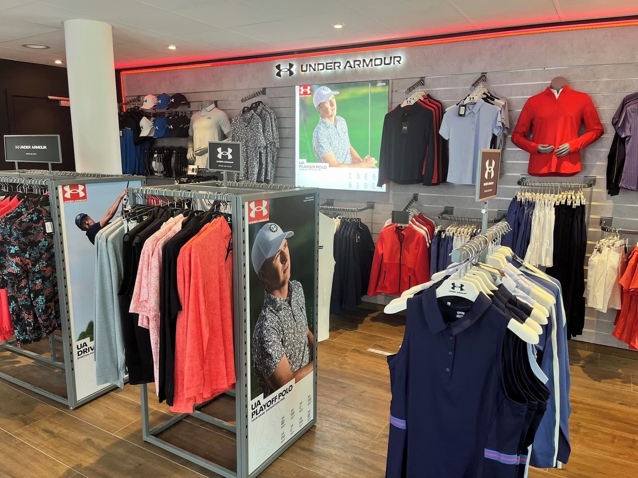 Una tienda de ropa con la marca Under Armour, que exhibe diversa ropa deportiva y de uso diario.