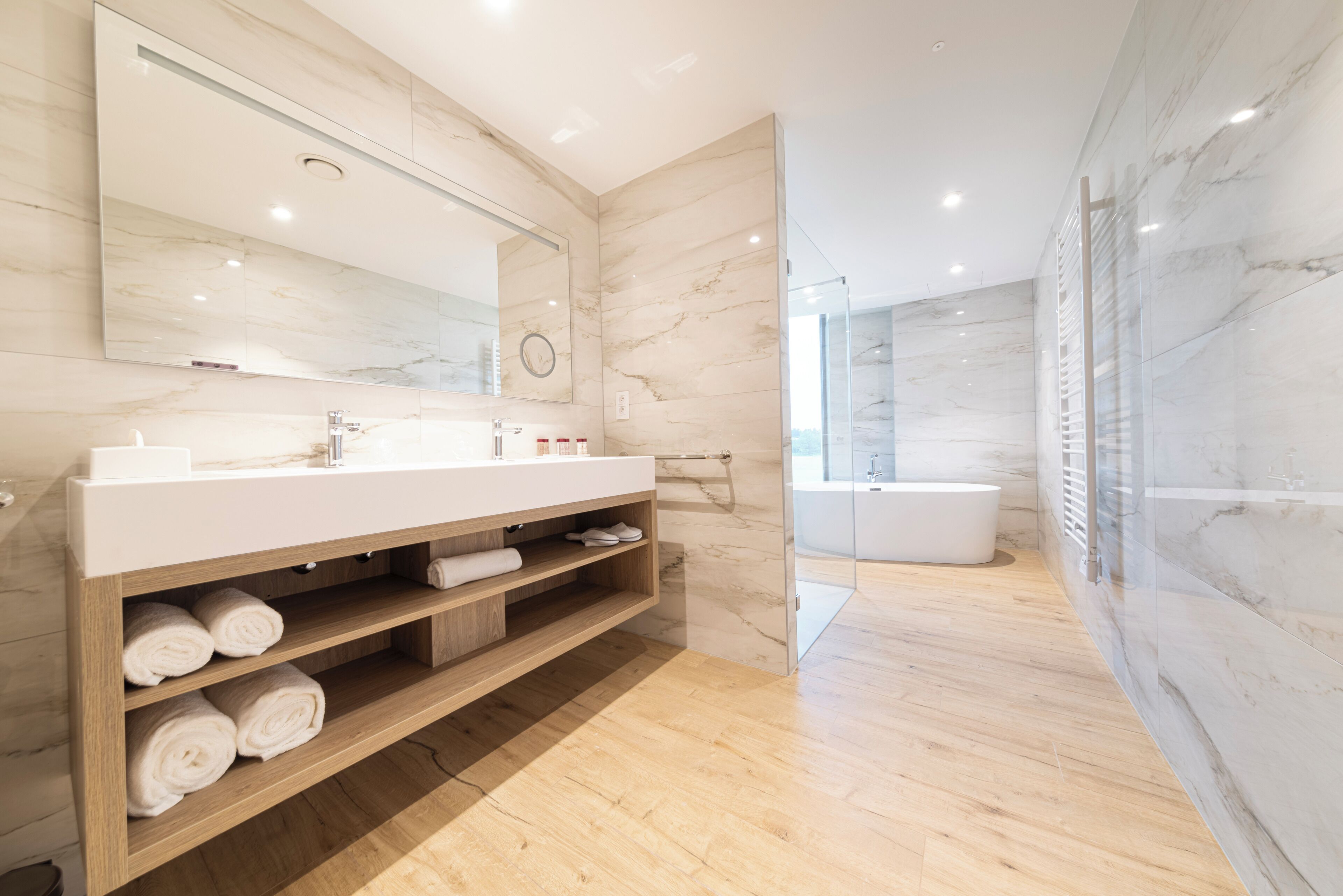 Een moderne badkamer met een grote spiegel, een houten wastafelmeubel en een bad.