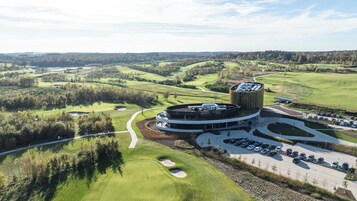 Un campo de golf con un edificio moderno de diseño circular, rodeado de exuberante vegetación y un aparcamiento.