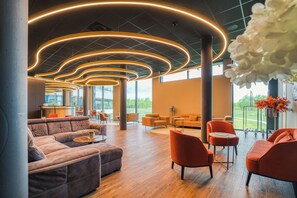Un vestíbulo espacioso con diseño moderno, que cuenta con un amplio espacio de estar con sofás y sillones, piso de madera y un techo con lámparas circulares.