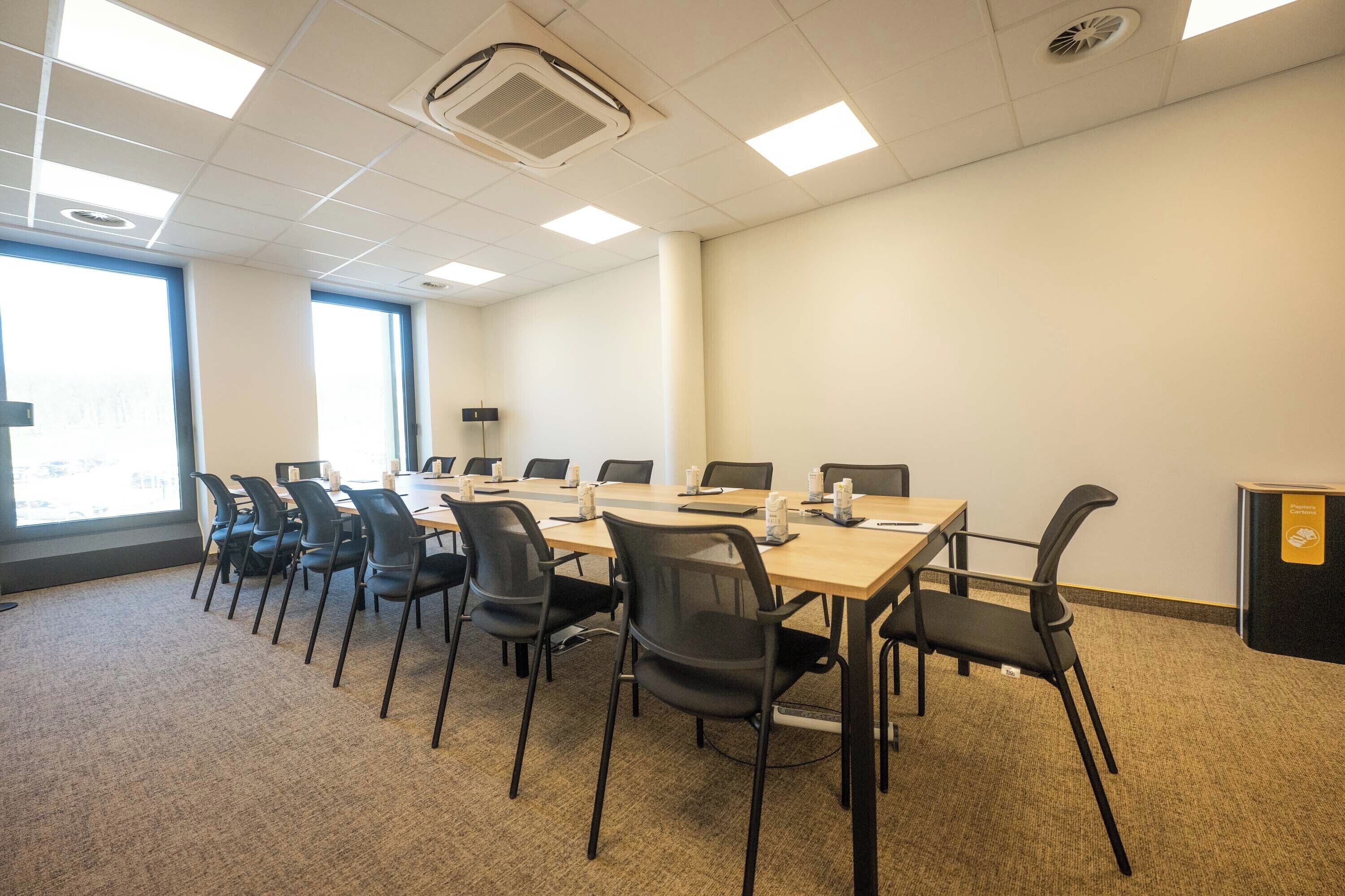 A conference room with a long table, black chairs, and a carpeted floor.