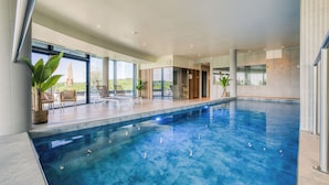 Une piscine intérieure moderne, avec une eau d’un bleu limpide, de grandes fenêtres et une vue sur l’extérieur.