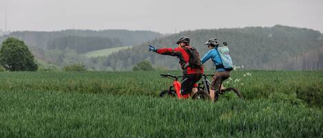 Two people on a mountain bike in a grassy field with a forested hill in the background.