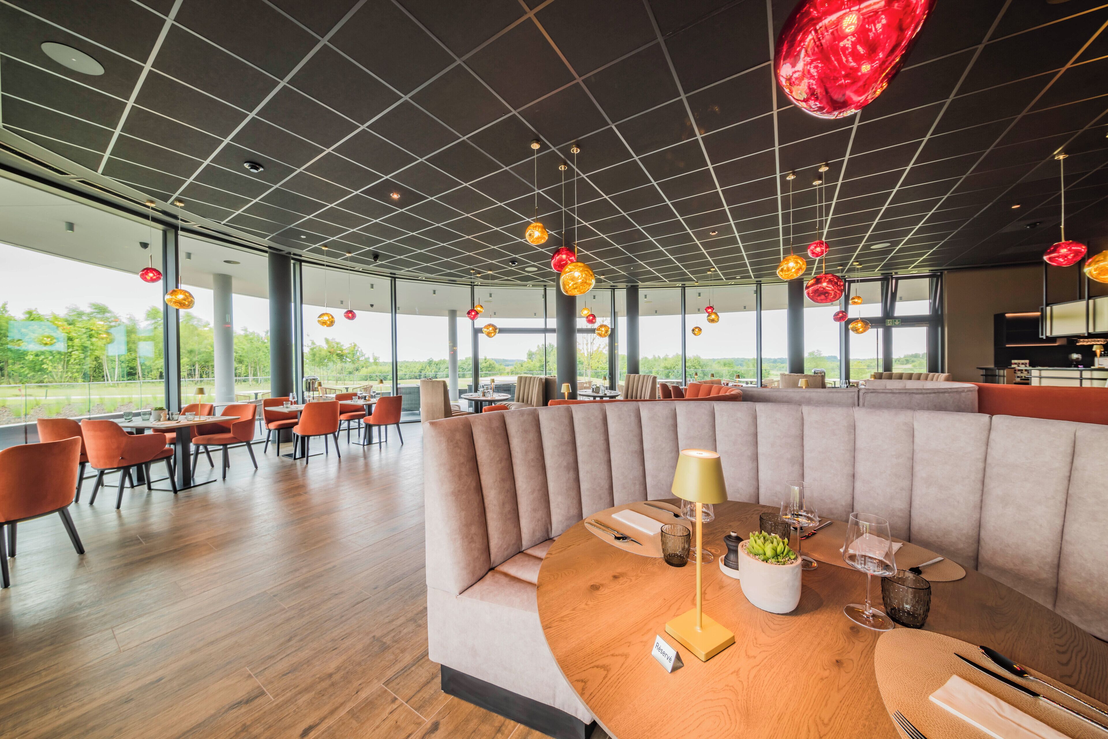 A modern restaurant with a curved seating area, large windows, and hanging pendant lights.
