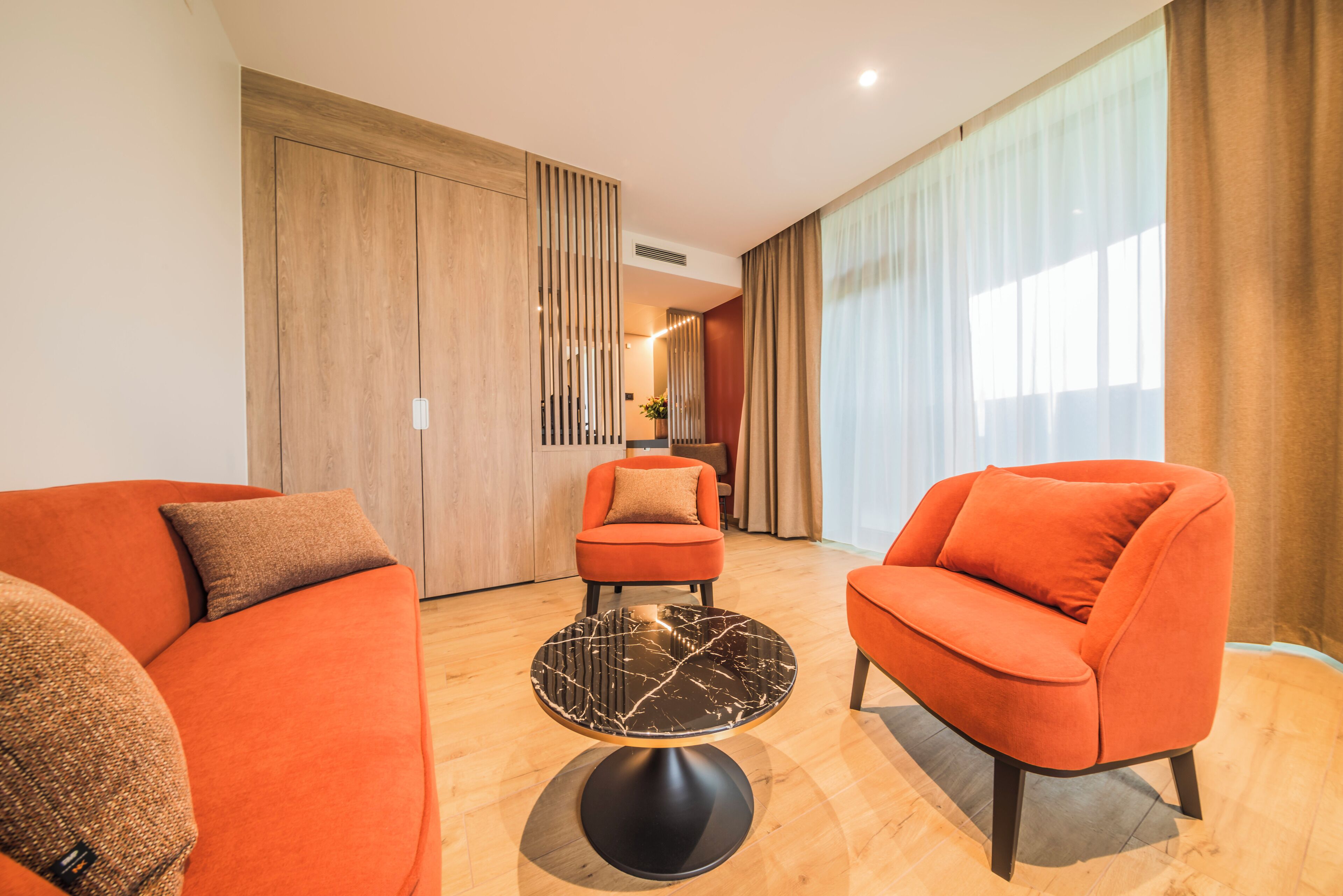 A modern living room with orange sofas, a black marble coffee table, and wooden flooring.