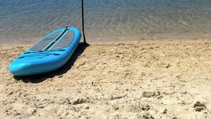 Un ciel d’un bleu limpide, une plage de sable et une planche de paddle bleu avec une pagaie noire.