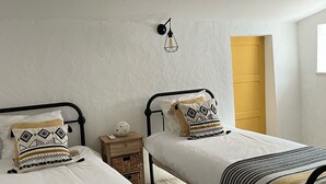 Une chambre avec deux lits, une table de chevet, une lampe et une porte.
