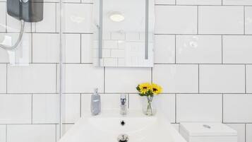 Un baño con un lavamanos blanco, un espejo y un cabezal de ducha.