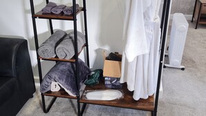 Una estantería de metal negro con toallas, una caja y un radiador blanco en una habitación con suelo de alfombra.