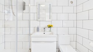Un baño moderno con baldosas blancas, cabina de ducha de vidrio, lavabo con espejo y un inodoro.