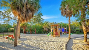 A sandy playground with swings, a slide, and a small wooden structure. - Turquoise Gem 1st Floor [no stairs] BEACH - TOP EATS - Longboat KeyFL (Longboat Key)