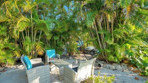An outdoor seating area with wicker furniture and a grill, surrounded by dense palm trees. - Turquoise Gem 1st Floor [no stairs] BEACH - TOP EATS - Longboat KeyFL (Longboat Key)