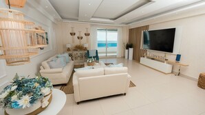 Un salon moderne avec un canapé blanc, un téléviseur et un balcon offrant une vue sur la mer.