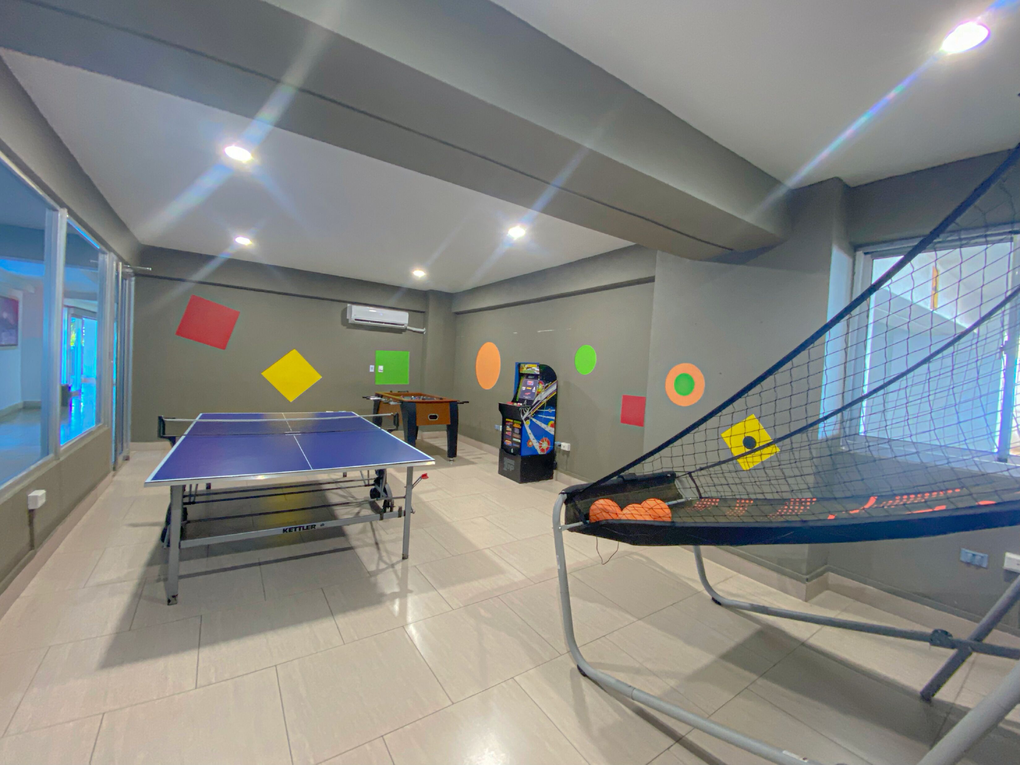 A recreational room with a ping pong table, a foosball table, and a trampoline.