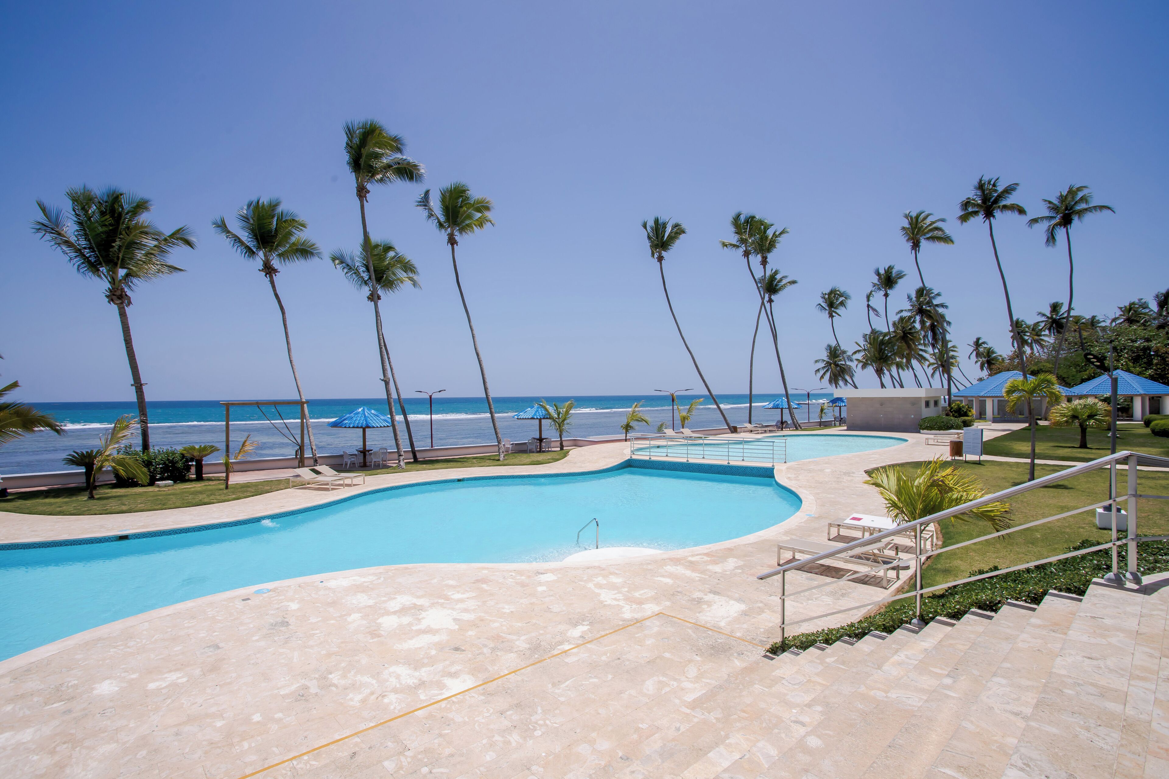 Une piscine avec vue sur l’océan, entourée de palmiers et bordée d’une plage.