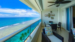 Un balcon avec vue sur l’océan, un ventilateur de plafond et un coin repas avec des chaises et une table.